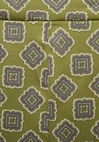 Tissu vert avec un motif de losanges répété, présentant des accents bleus, crème et marron, délimités par des bords en forme de vagues. Surface lisse et texturée.