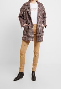 Ruudullinen oversized takki punaisena, mustana ja valkoisena, taskuilla, kerroksittain valkoisen T-paidan päällä. Yhdistetty vaaleisiin housuihin ja mustiin nilkkakorkoihin.