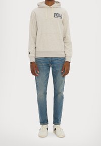 Světlě šedá mikina s kapucí, přední kapsou typu klokánek a šňůrkami, na přední straně tmavě modré vyšívané logo "Polo". Kombinováno s modrými džínami.