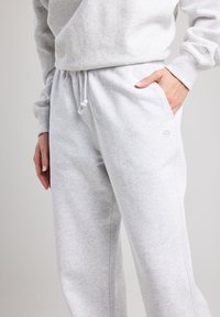 Pantaloni della tuta grigi realizzati in tessuto morbido, con tasche laterali, un elastico in vita con cordino e un piccolo logo vicino alla tasca.