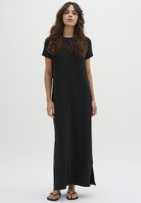Black maxi dress with short sleeves, smooth texture, side slits for ease, and minimalist design. Paired with black flip-flops.