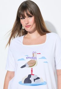 T-shirt blanc avec un décolleté carré, présentant un graphique coloré d'une mouette portant une écharpe rayée, se tenant sur un rocher avec des nuages.