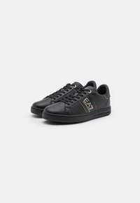 Black leather sneakers with gold accents, round toe, lace-up design, and rubber sole. Features a logo on the side and minimal stitching details.