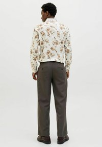 Wit shirt met bloemenpatroon en beige accenten, lange mouwen. Donkergrijze broek met achterzakken, gecombineerd met bruine schoenen.