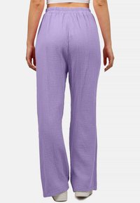Lichtpaarse, gestructureerde broek met een elastische tailleband en wijduitlopende pijpen, van de achterkant weergegeven. Materiaal heeft een gekreukt uiterlijk.