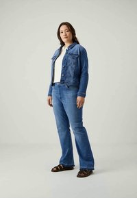 Τζάκετ από τζιν και φαρδιά τζιν παντελόνια σε μεσαίο μπλε, συνδυασμένα με λευκό μπλουζάκι και μαύρες σάντες. Περιλαμβάνει κουμπωτές τσέπες και ραφές.