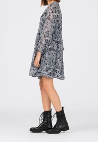 Kukkakuosiset, puolipeittäviä A-linjan mekko tummansinisessä ja harmaassa, jossa on pitkät hihat ja poimuinen vyötärö, yhdistetty mustiin nauhakiinnitteisiin taistelukenkään.