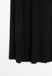 Gonna plissettata nera in tessuto morbido, con pieghe verticali e design fluido, dalla texture liscia e orlo uniforme.