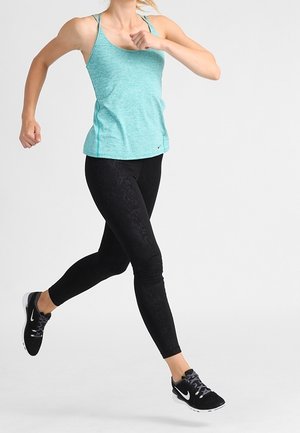 Débardeur turquoise clair à fines bretelles, associé à des leggings noirs à motifs. Modèle en mouvement, portant des chaussures de sport noires.