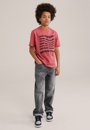 Korte mouwen roze T-shirt met zwarte tekst "BLUE RIDGE DENIM", gecombineerd met grijze jeans en zwart-witte sneakers. Soepele stof, casual fit.