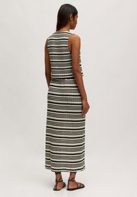 Schwarz-weiß gestreiftes Zweiteiler-Outfit mit einem ärmellosen Cropped-Top und einem langen Rock. Strukturierter Stoff mit tailliertem Schnitt und flachen Sandalen.