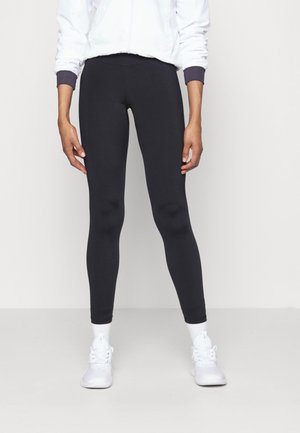 Zwarte leggings van rekbare stof, met een aansluitend ontwerp dat tot de enkels reikt, gecombineerd met witte sportschoenen en sokken.