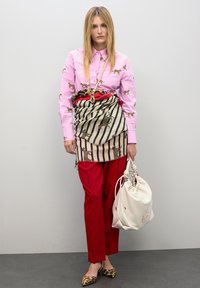 Camisa rosa con estampado animal, falda envolvente estampada, pantalones rojos, bailarinas con estampado animal y una bolsa blanca con cuerda. Texturas suaves y colores audaces.