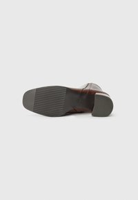Brown leather boot featuring a rounded toe, textured gray rubber sole, low heel, and minimal stitching details.