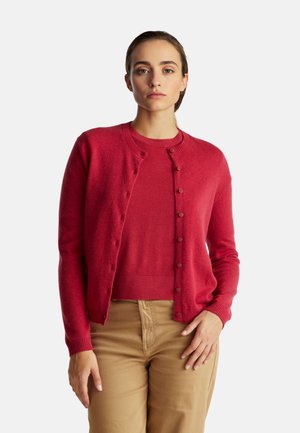 Rode wollen cardigan met een ronde hals, knoopsluiting en geribde manchetten, gedragen over een bijpassend rood topje en beige broek.