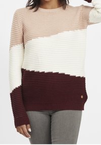 Sweter dziergany z blokowym wzorem w kolorach beżowym, kremowym i bordowym. Teksturowana tkanina z prążkowanymi mankietami i małym akcentem w postaci logo.