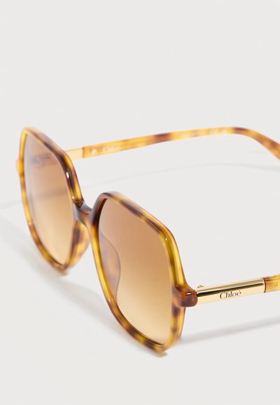 Lunettes de soleil hexagonales en écaille de tortue avec verres dégradés marron et accents dorés ornés du logo Chloé sur les branches.