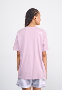 Kurzarm-T-Shirt mit Rundhals in Hellrosa, mit einem kleinen weißen Logo im oberen Rückenbereich. Der Stoff wirkt weich und hat einen lässigen Schnitt.