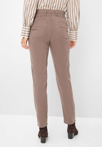 Bruine op maat gemaakte broeken met een gladde textuur, voorzien van achterzakken en een hoge tailleband, gecombineerd met donkere enkelboots.