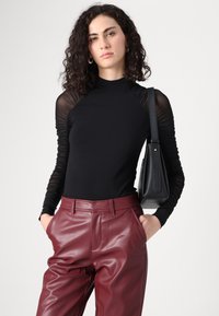 Haut noir à manches longues avec des manches transparentes texturées, associé à un pantalon en cuir bordeaux taille haute. Accessoirisé avec un petit sac noir.