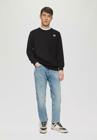 Zwart sweatshirt met witte kraag en logo, lichtblauwe spijkerbroek en eenkleurige sneakers. Eenvoudig ontwerp en ontspannen pasvorm.