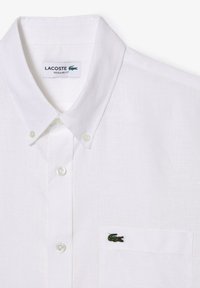 Camicia bianca con bottoni realizzata in tessuto strutturato, dotata di colletto classico e tasca con logo di coccodrillo verde. Design a vestibilità regolare.