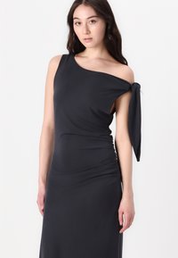 One-shoulder black dress with a tied detail at the shoulder. Features a fitted silhouette and ruched texture along the side. Smooth fabric.