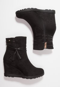 Stivali alla caviglia con tacco a cuneo neri in suede, dotati di zip laterale, cinturini decorativi con nappine e suola in gomma con grip testurizzato.