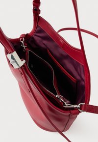 Czerwona skórzana torebka na ramię z główną kieszenią zapinaną na zamek, kieszeniami wewnętrznymi oraz srebrnymi metalowymi akcentami. Gładka faktura z błyszczącym wykończeniem.
