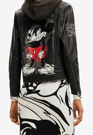 Czarna skórzana kurtka z dużą grafiką w stylu vintage Myszki Miki na plecach i napisem „Mickey Mouse” na rękawie, noszona na czarno-białej spódnicy w wzory.