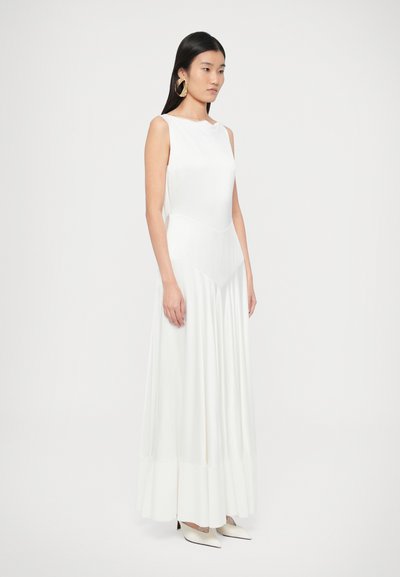 Balta maxi suknelė be rankovių, su prigludusiu liemeniu, platėjančia sijono dalimi ir siūlių detalėmis. Lygus audinys su švelniu blizgesiu, derinamas su smėlio spalvos aukštakulniais.