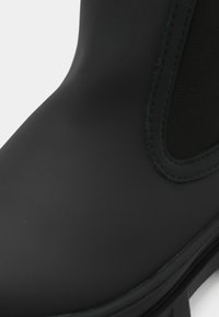 Botte en caoutchouc noir avec une surface lisse, des panneaux latéraux élastiques et une semelle texturée, conçue pour la durabilité et le confort.