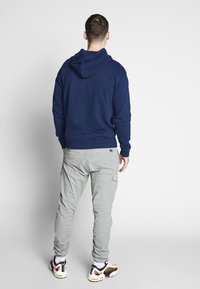 Tmavě modrá mikina s kapucí, doplněná světlými šedými kalhotami s kapsami. Outfit je dokončen vícebarevnými sportovními botami.