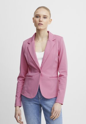 Světle růžový blazer s klopami, zapínání na jeden knoflík, dvě přední kapsy a hladká textura, nošený přes bílou halenku a modré džíny.