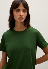 Grünes Baumwoll-T-Shirt mit Rundhalsausschnitt und kurzen Ärmeln. Glatte Textur, lässige Passform und minimalistisches Design ohne Muster oder Akzente.