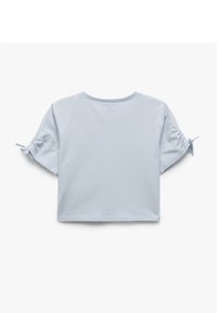 Top corto de algodón azul claro con mangas cortas que presenta detalles fruncidos en los puños y un escote redondo. Textura suave.