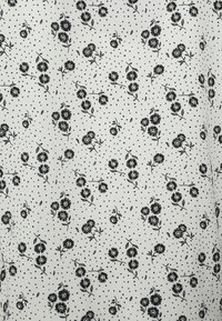 Padrão floral preto sobre tecido branco, com pequenos pontos pretos espalhados por toda a parte. O design apresenta flores e folhas em detalhes finos.