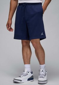Marineblå sports shorts med elastisk talje og snørebånd, med et hvidt Jumpman-logo på siden. Parret med hvide og grå sneakers.