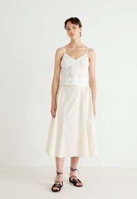 Vitt broderat bodice-top med tunna axelremmar, tillsammans med en flödande elfenbensfärgad kjol och svarta sandaler med remmar. Enkelt och minimalistisk design.