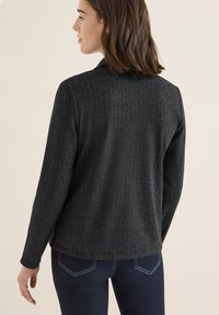 Sort skjortefrakke i herringbone med lange ærmer og slagkrave. Stoffet ser teksturelt ud; sat sammen med mørkeblå jeans.