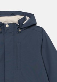 Vodoodporna mornarsko modra jakna s kapuco, ki ima sprednjo zapenjanje na sponke, elastične zapestnice in mehko podlogo. Vključuje sprednji žep kot podrobnost.