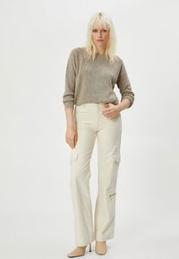 Beige gestrickter Pullover kombiniert mit cremefarbenen weiten Cargo-Hosen mit Seitentaschen und Reißverschlussakzenten. Das Model trägt beige spitze Pumps.