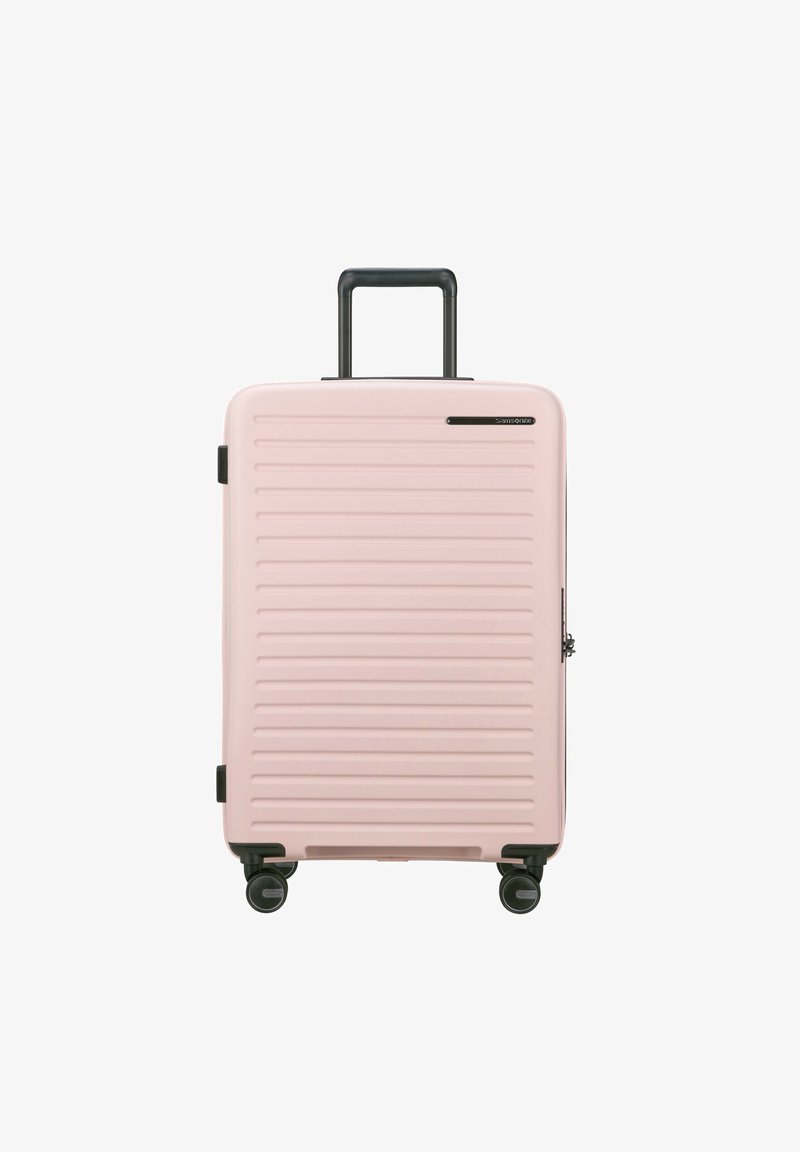 Pink hard-shell suitcase with vertical grooves, retractable black handle, and four spinning wheels for mobility. Zipper closure, compact design.