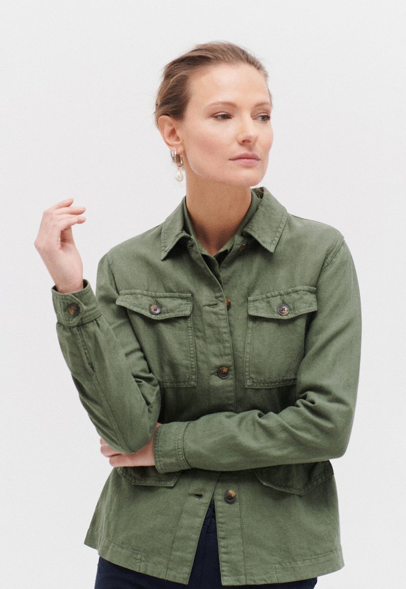 Veste verte à boutons, fabriquée en tissu léger, avec deux poches poitrine, un col et des manches à poignets. Le design présente une coupe décontractée.