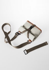 Borsa a tracolla piccola e rettangolare in materiale grigio chiaro con dettagli in pelle marrone. Caratterizzata da spallacci regolabili e una fibbia per la chiusura.