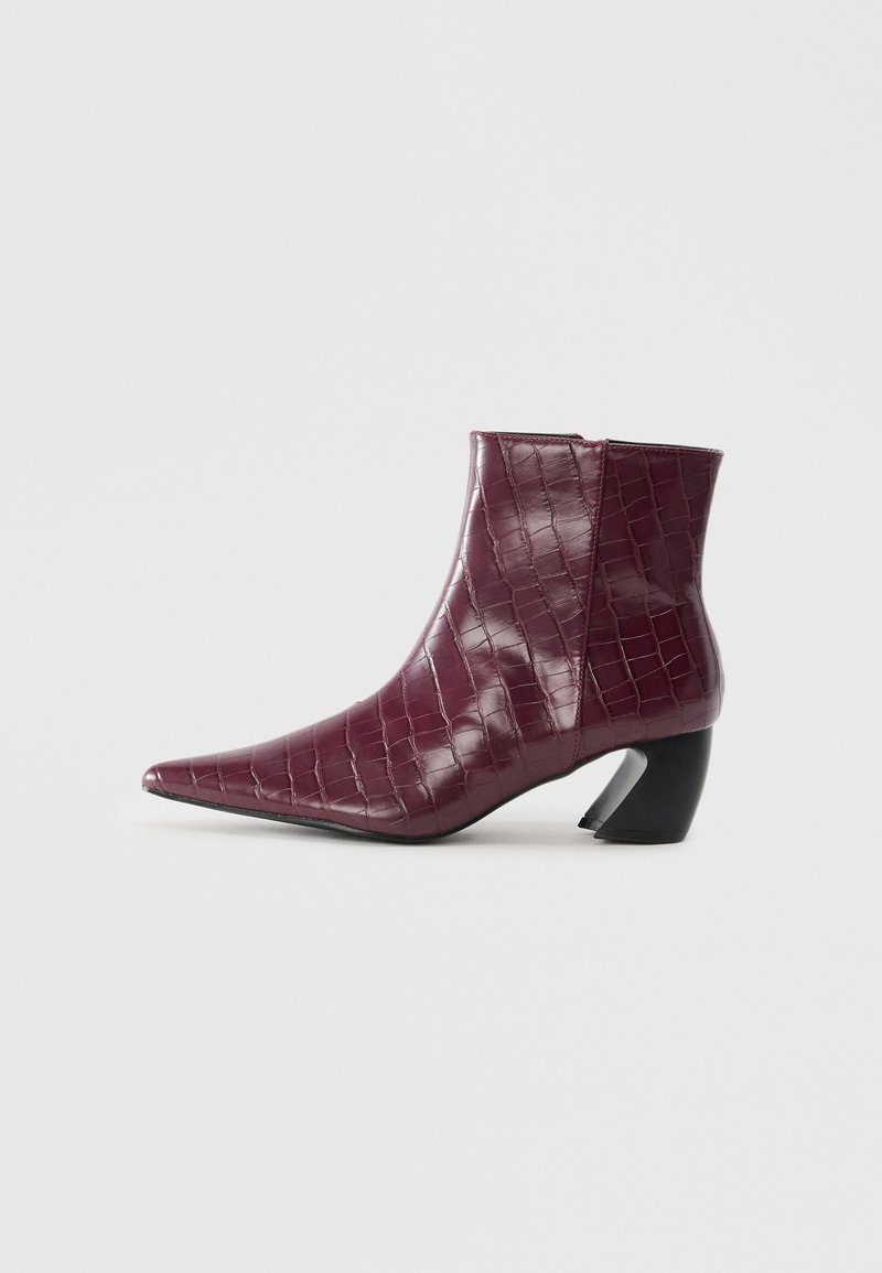 Stivaletto bordeaux con texture di coccodrillo, punta appuntita e tacco a blocco nero curvo su sfondo bianco semplice.