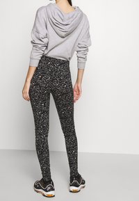 Šedá mikina s kapucí v kombinaci s černými legínami se bílým abstraktním vzorem. Černé sportovní boty s žlutými akcenty.