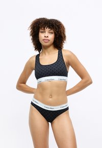 Sort sports-bh og trusser sæt, med et geometrisk mønster og Calvin Klein-logo på elastiske bånd. Glat tekstur, tætsiddende pasform.