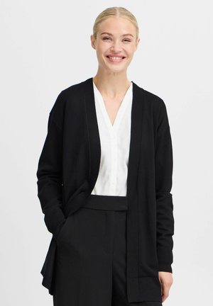 Black cardigan with long sleeves, open front design, and soft texture, layered over a white shirt, paired with black trousers.