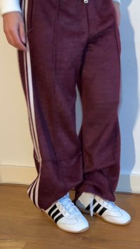 Person som bär vinröda träningsbyxor med vita ränder och vita sneakers med svarta ränder, står på ett trägolv.